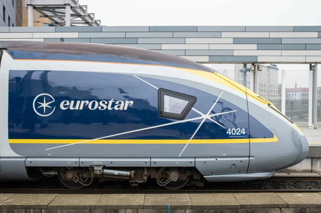 Side profile close-up of a modern blue, yellow, and grey Eurostar high-speed train car numbered 4024 stopped on a track at a station platform.