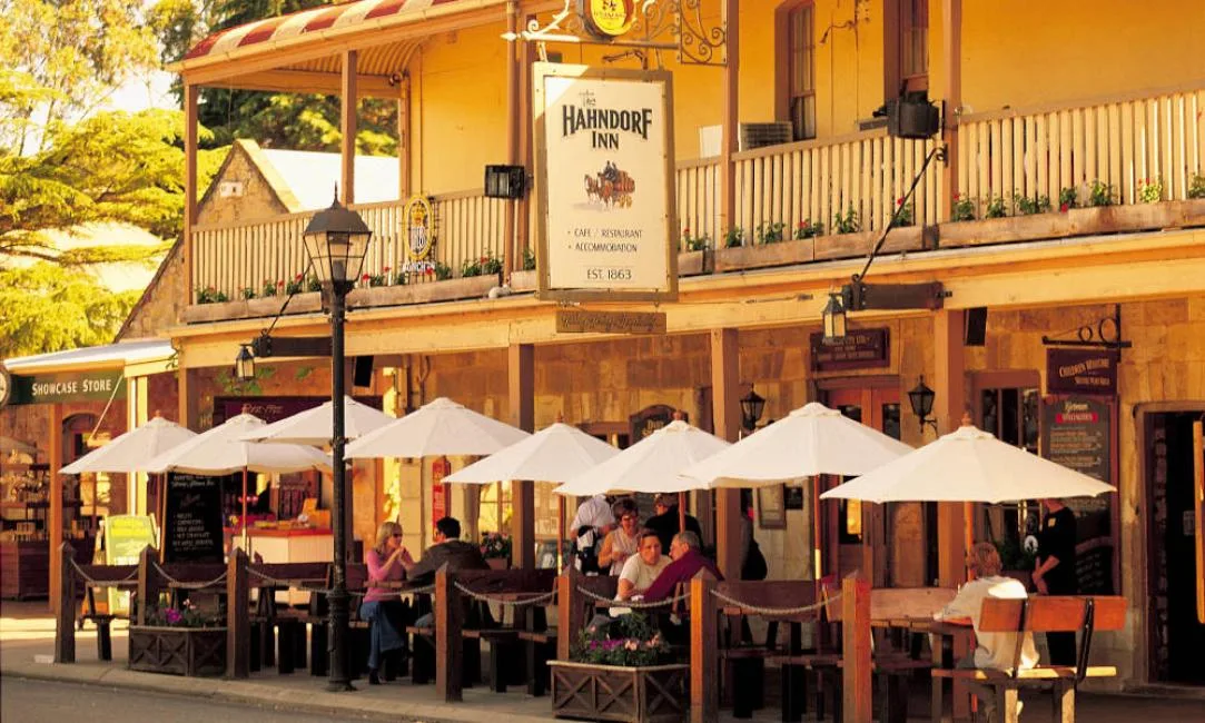 People dine at outdoor tables under white umbrellas in front of the historic stone facade of the Hahndorf Inn.
