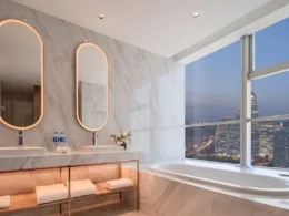 Modern marble bathroom featuring a double vanity with oval mirrors and a bathtub overlooking the Beijing city skyline at night.
