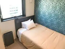 A compact and clean single room at Hotel LiVEMAX Ikebukuro Ekimae featuring a bed with a tan duvet and white pillows.