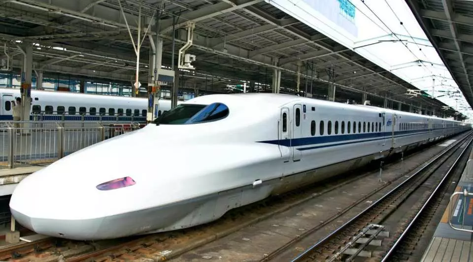 A white Shinkansen N700 series bullet train with a blue stripe stopped at a Japanese railway station platform