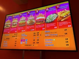 Digital menu board at Krusty Burger in Universal Studios featuring a variety of burgers, a chicken caesar salad, hot dogs, and specialty beverages like Buzz Cola and Squishees