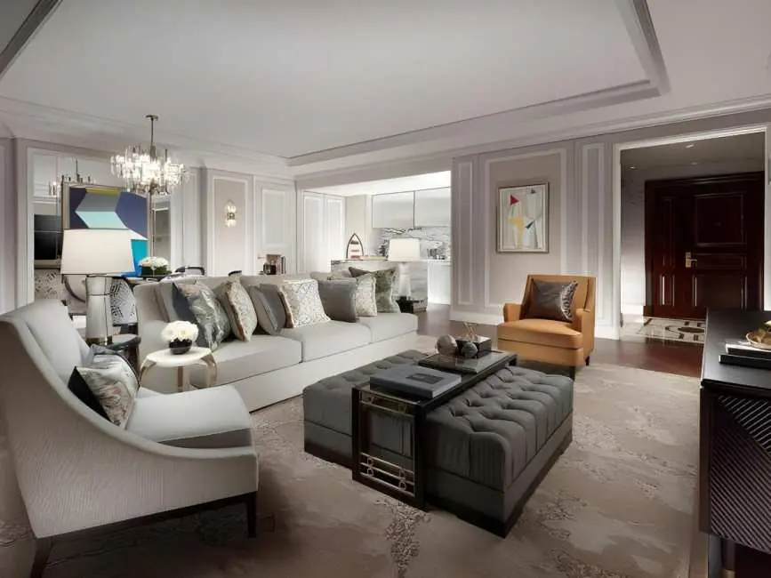 A luxurious, modern hotel suite with a large grey sectional sofa, tufted ottomans, and elegant neutral-toned deco