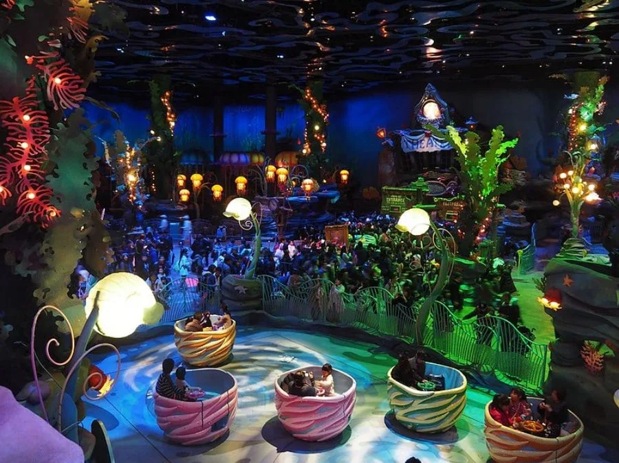 Visitors riding spinning seashell attractions inside the illuminated underwater-themed Mermaid Lagoon area at Tokyo DisneySea.