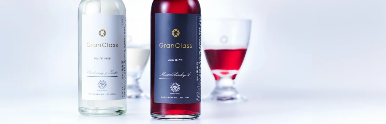 Two bottles of Gran Class wine, one white and one red, displayed with their respective glasses on a clean, bright white background.
