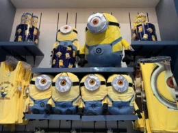A retail display shelf at a theme park featuring various Minions merchandise