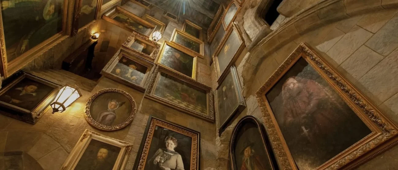 An upward view of a high stone wall covered in numerous ornate framed talking portraits inside the Hogwarts Castle queue for Harry Potter and the Forbidden Journey at Universal Studios Hollywood