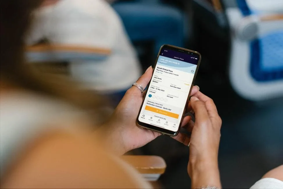 A person holds a smartphone displaying a digital Eurail Global Pass mobile ticket while sitting on a train.