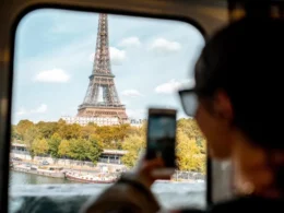 a traveler looking through a train window to capture a smartphone photograph of the Eiffel Tower in Paris, France.