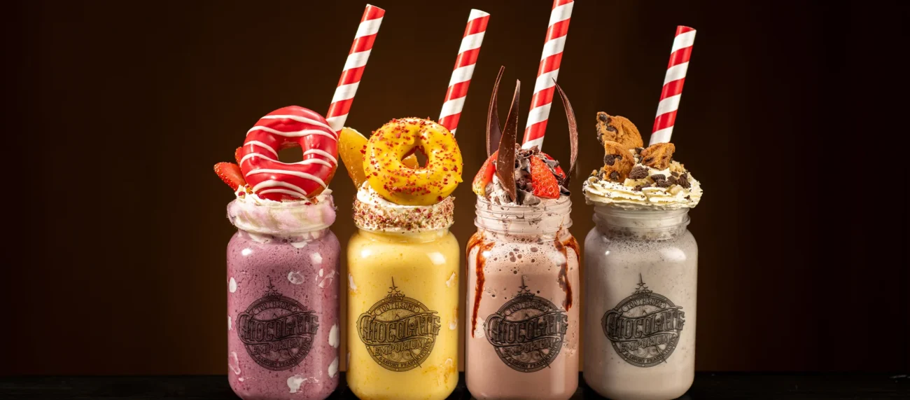 Four elaborate milkshakes from Toothsome Chocolate Emporium topped with donuts, cookies, and whipped cream in mason jars.