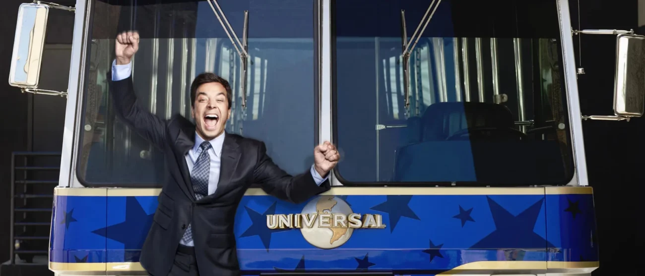 A life-sized cutout of a cheering Jimmy Fallon leaning against the front of a blue and gold Universal Studios tour tram