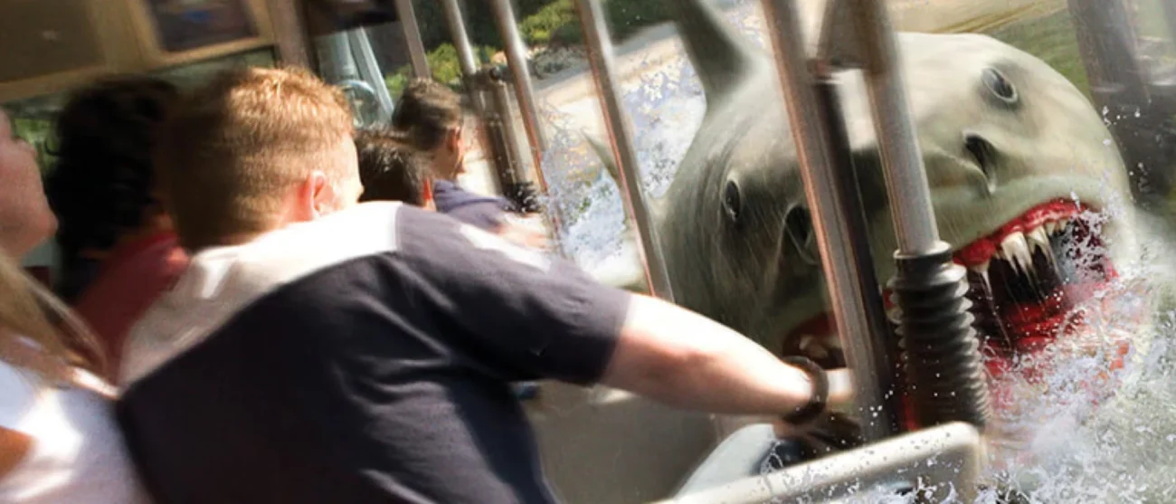 An animatronic great white shark with open jaws emerging from the water next to a Universal Studios Hollywood tour tram