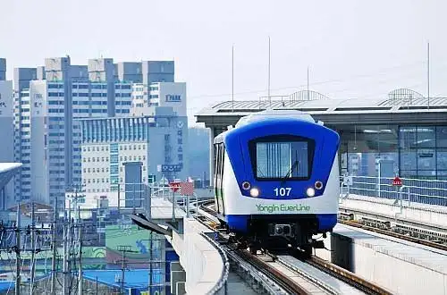 A blue and white Yongin EverLine subway train traveling on elevated tracks with city buildings in the background.